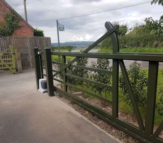 A 5 bar metal gate with automation at an angle, painted in dark green