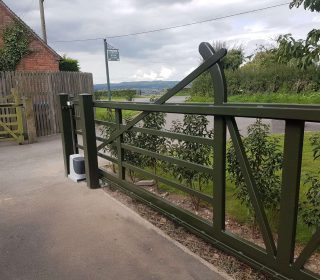 A 5 bar metal gate with automation at an angle, painted in dark green